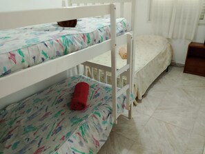 A bunk bed with a patterned mattress, a small wooden nightstand, and a window with blinds. - Apartment Club Nautico (Los Nietos)