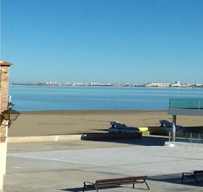 A beach view with a clear sky, a sandy beach, and a distant cityscape.