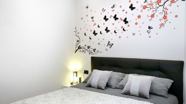 A bedroom with a bed, pillows, a nightstand, a lamp, and a wall with a nature-themed decal.