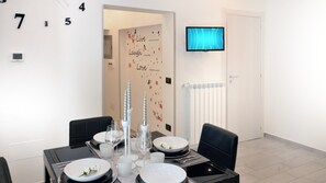 A dining area with a table set for four, a television mounted on the wall, and a door with a decorative wall decal. - HOME SWEET HOME (Napoli)