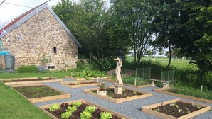 A garden with raised beds, a stone building, and a statue. - Luxury Family Farmhouse, Pool and Games Room. Perfect for DDay, Mont st Michel (Le Mesnil-Garnier)