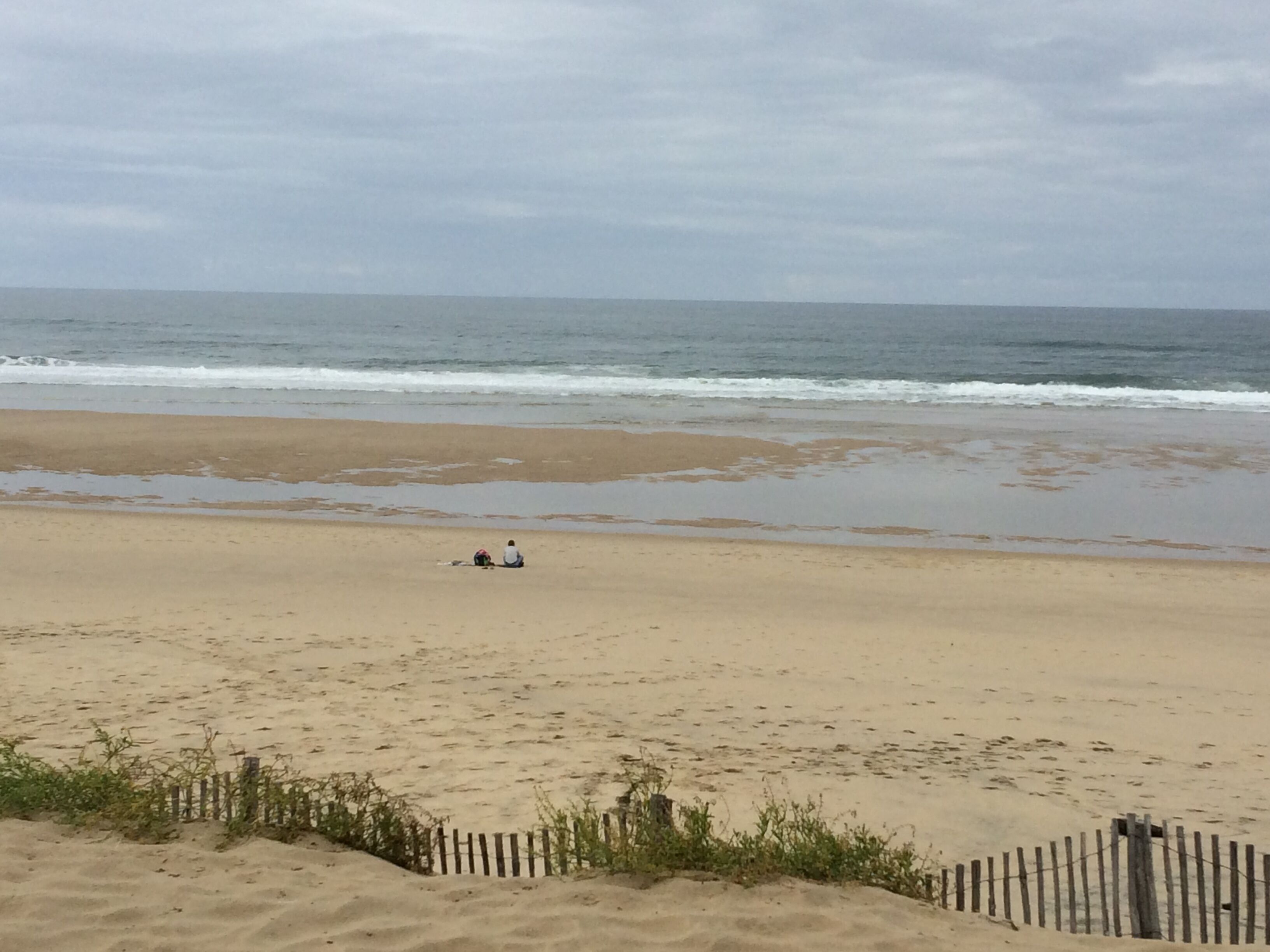 Une plage avec une clôture en bois et une personne assise sur le sable.