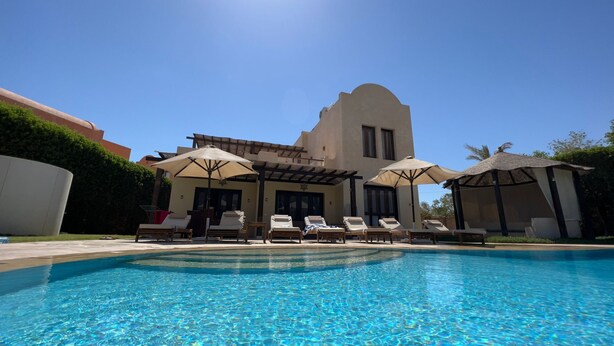 A poolside area with lounge chairs and umbrellas, a clear blue pool, and a building with a unique architectural design. - Extremely private villa with own pool (heating optional) - sleeps up to 6 (El Gouna)