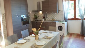 Cozinha moderna com eletrodomésticos embutidos, sala de jantar com mesa posta para quatro pessoas e máquina de lavar roupa.