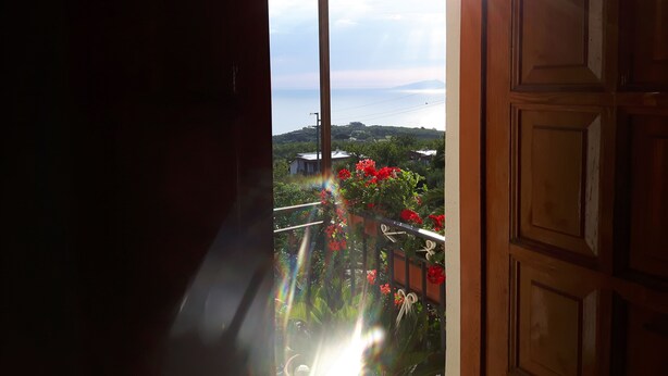 Uma varanda com vista para o mar e montanhas, uma porta de madeira e um corrimão com flores.