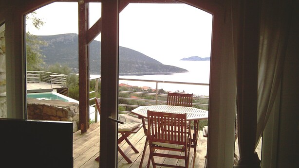 A wooden deck with a table and chairs, overlooking a pool and a scenic view of mountains and water. - Melolia A2 holiday home with pool and fabulous views (Alyki)