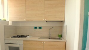 Une cuisine compacte avec des meubles en bois, une cuisinière à gaz, un évier et un égouttoir vert.