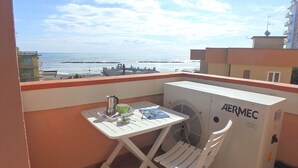Un balcon avec une table, des chaises, un ventilateur et une vue sur la mer.