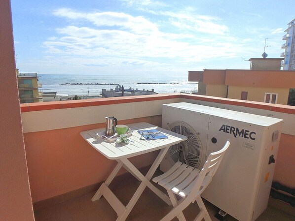 Un balcon avec une table, des chaises, un ventilateur et une vue sur la mer.