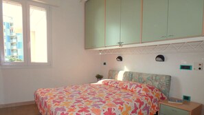 A bedroom with a bed, a window, a green wardrobe, a bedside table, and a wall-mounted thermostat. - Large three-room apartment in the center with beautiful sea view in Lido di Pomposa (Lido di Pomposa)