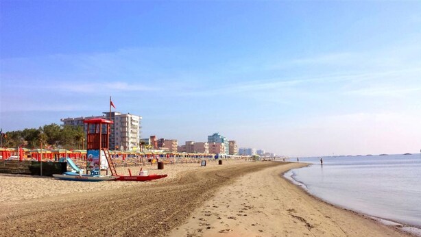 Une plage avec une tour de surveillance, des parasols et une rangée de bâtiments en arrière-plan.