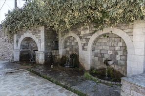 Stunning arched fountains set within a stone wall, surrounded by lush greenery and stone tiles.