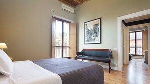 A hotel room with a bed, a bench, a framed picture, and a door leading to another room.