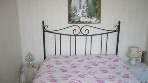 Un dormitorio con cabecera de metal, cama con colcha estampada de flores, mesita de noche con lámpara y un cuadro de una cascada en la pared.