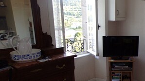 Una habitación con un aparador de madera, un televisor sobre un mueble bajo, una ventana con vistas a un paisaje verde y un espejo.