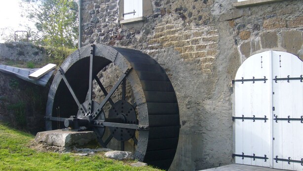 Un edificio de piedra con una gran noria de agua y una puerta blanca con bisagras negras.