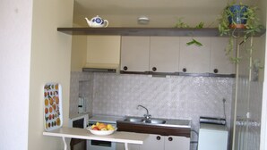 Una cocina compacta con cubierta blanca, un cuenco de fruta, microondas y un lavamanos.