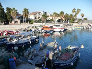 A marina with various boats docked, a sandy beach, and buildings in the background. - the small beach, studio (Cagnes-Sur-Mer)