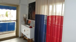 Una habitación con un tocador blanco, una computadora portátil, una lámpara y vistas a un balcón azul.