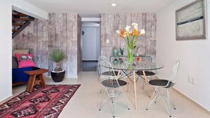 Un salon moderne avec une table à manger en verre, des chaises en métal, un tapis rouge à motifs, une plante en pot et un escalier.