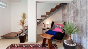 Un salon moderne avec un escalier, un lit avec une literie aux couleurs vives et deux plantes en pot.