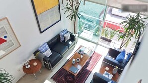 Un salon moderne avec un canapé noir, une table basse et une vue sur la mer grâce à de grandes fenêtres.