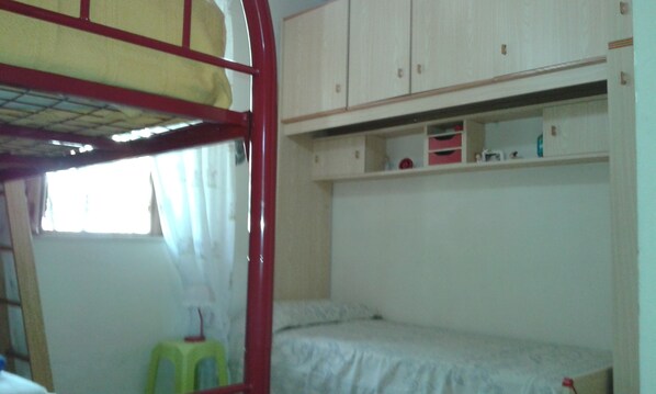 Habitación con literas, una ventana, un taburete pequeño y una estantería con objetos.