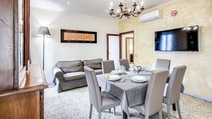 A dining area with a table set for six, a sofa, a chandelier, and a TV mounted on the wall. - Times Rome Colosseum, wide in wonderful location front Coliseum (Rome)