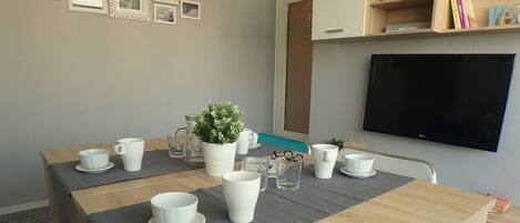 Un coin repas avec une table dressée pour quatre personnes, une plante en pot et un téléviseur à écran plat fixé au mur.