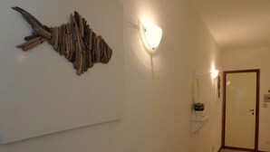 A room with a wall-mounted fish sculpture, a wall sconce, a door, and a small potted plant on a shelf. - Sea view, bright apartment in the center of Lido di Pomposa (Comacchio)