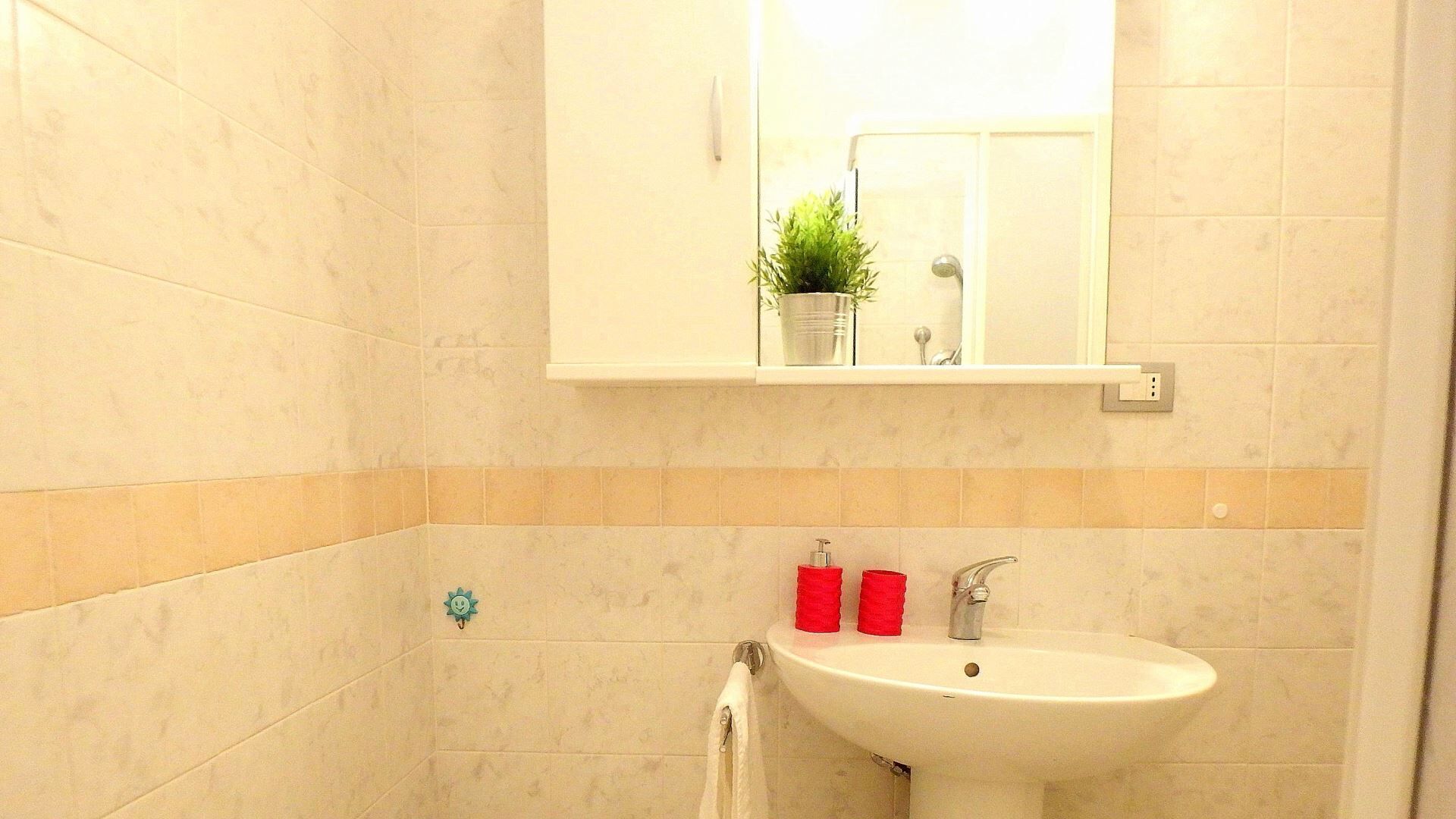 Un baño con un lavamanos blanco, artículos de tocador rojos y un espejo encima.