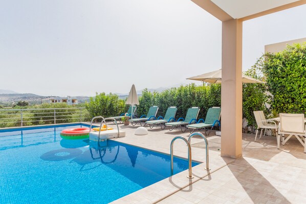 A swimming pool with lounge chairs and a table, surrounded by greenery and a view of the landscape.