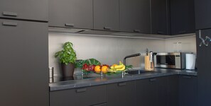 A modern kitchen with dark cabinets, a stainless steel sink, a microwave, and a fruit bowl with bananas, oranges, and apples.