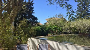 Un espacio al aire libre con dos sillas, una mesa, una piscina de concreto y vegetación circundante.