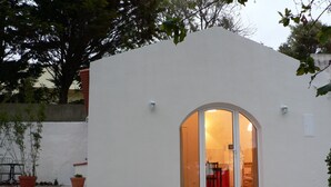 Un edificio blanco con un amplio arco de entrada que da a un espacio interior con una silla roja y una mesa.