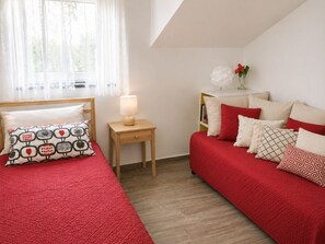 A bedroom with a bed, a nightstand, a lamp, a sofa, and a window with curtains.