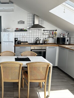 A modern kitchen with white tiles, a gas stove, a microwave, and a dining area with wicker chairs.