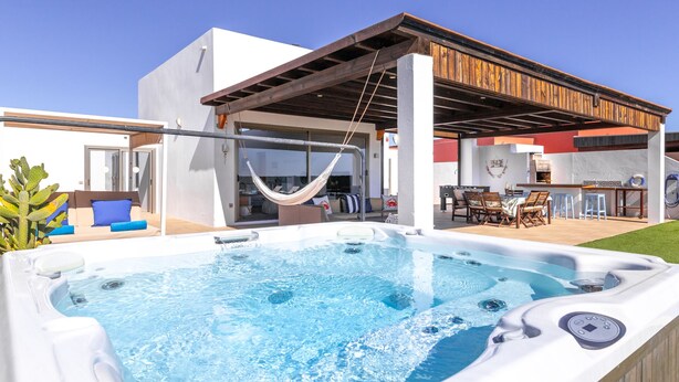 A modern outdoor pool area with a hot tub, a covered seating area, and a barbecue setup.