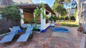 Ein Patio mit Whirlpool, Liegestühlen und einer Pergola mit Weinreben.