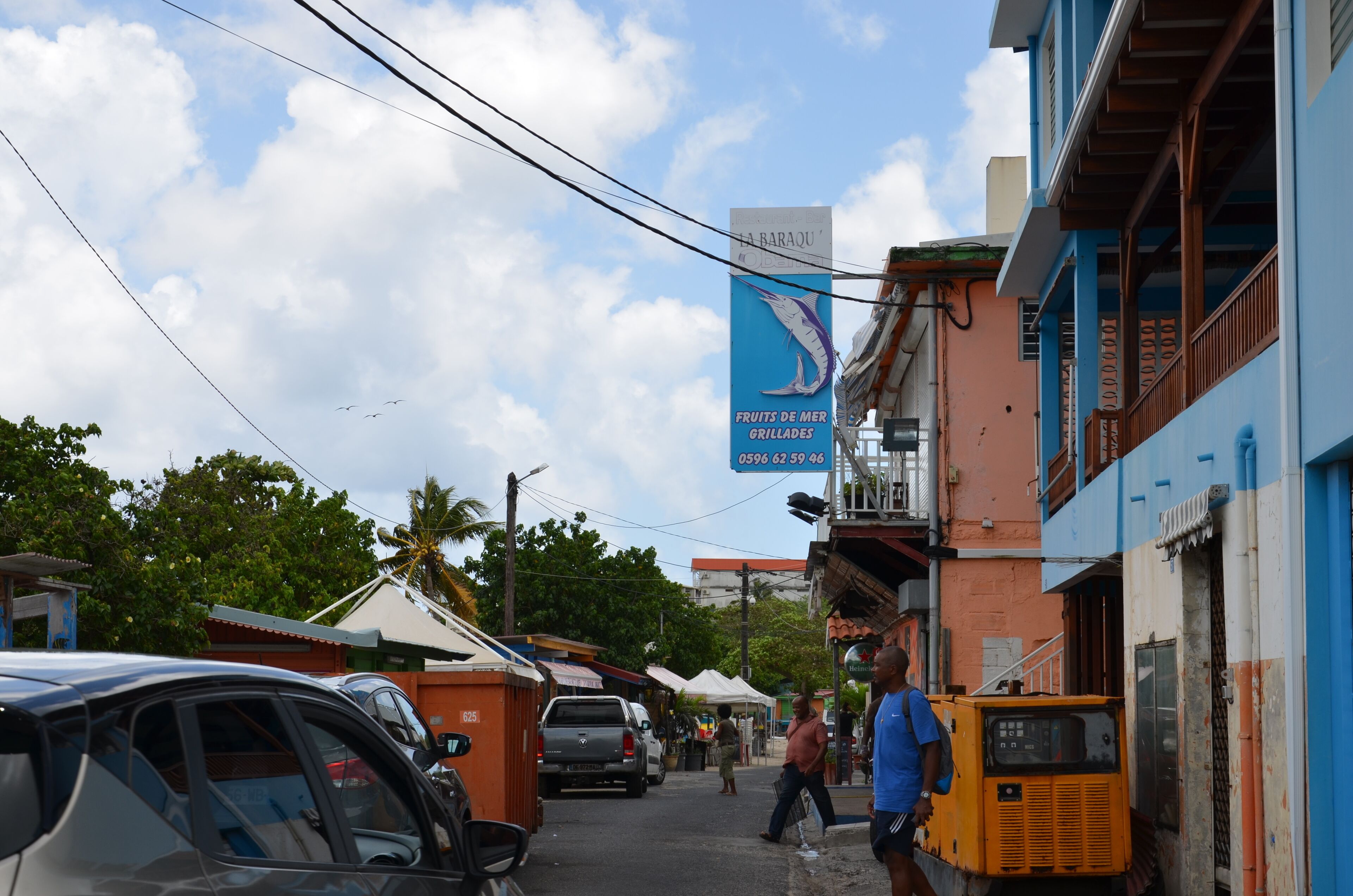A street view with parked cars, a blue building with a sign for a restaurant, and a yellow vehicle.