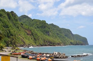 Escena costera con barcos, costa rocosa y una exuberante montaña verde.