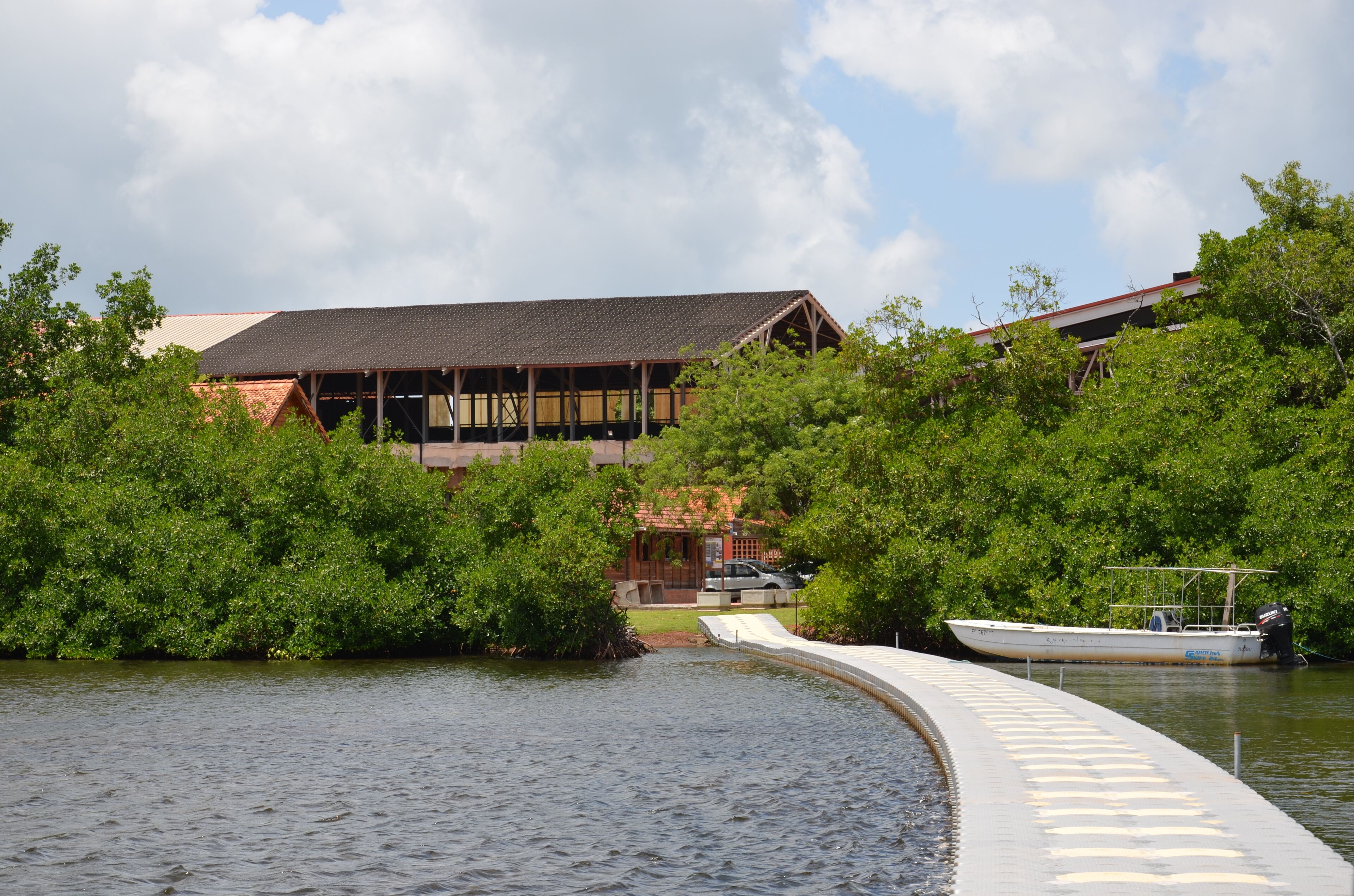 A building with a sloped roof, surrounded by lush greenery and a body of water.