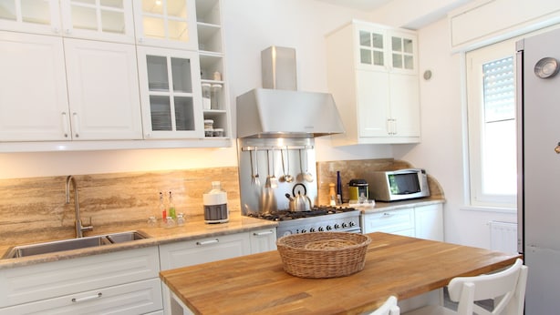A kitchen with white cabinets, a wooden table, and a stainless steel range hood. - Family House (Cefalù)