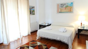A hotel room with a bed, a nightstand, a lamp, a painting, and a window with curtains. - Family House (Cefalù)
