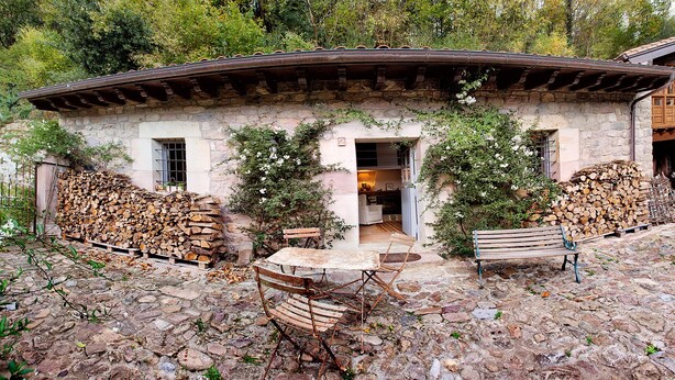 A rustic stone building with a stone roof, a wooden bench, and a pile of firewood.