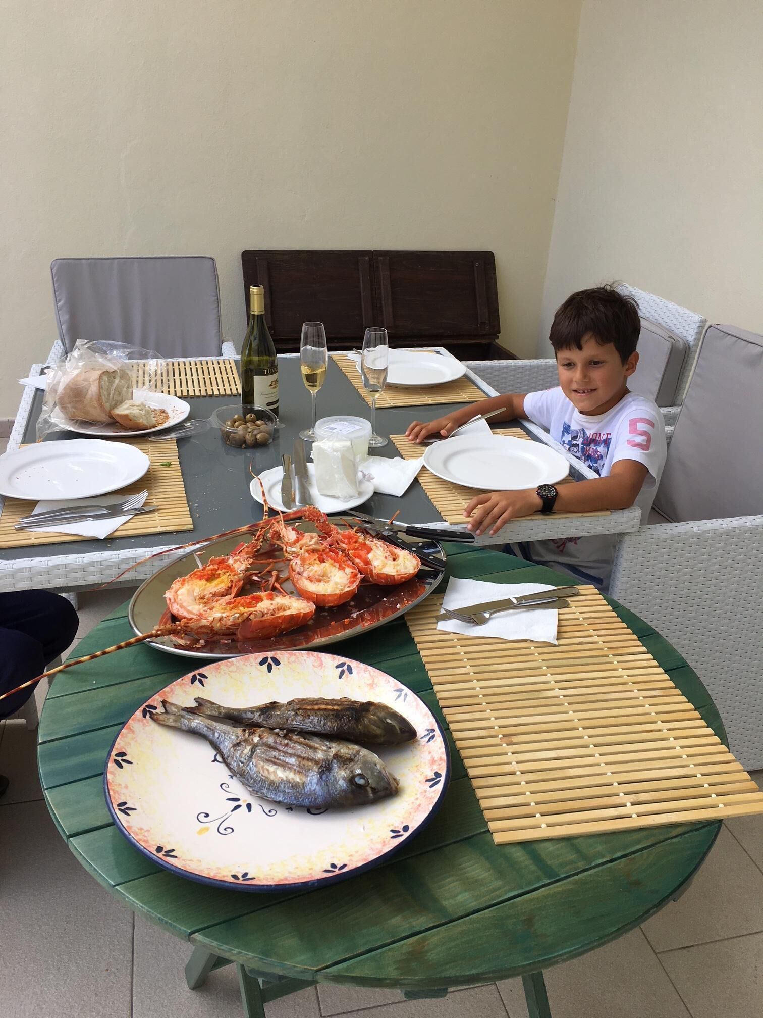 A dining table with seafood dishes, a bottle of wine, and a child seated at the table.