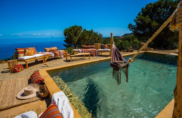 A poolside area with lounge chairs and a hammock, overlooking a clear blue sea.