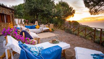 Guests can enjoy a peaceful outdoor seating area with a stone building backdrop, surrounded by lush greenery and a wooden fence.