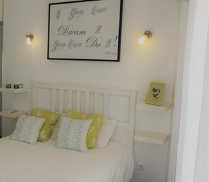 A neatly arranged bedroom with a bed, pillows, a bedside table, and a wall-mounted sign.