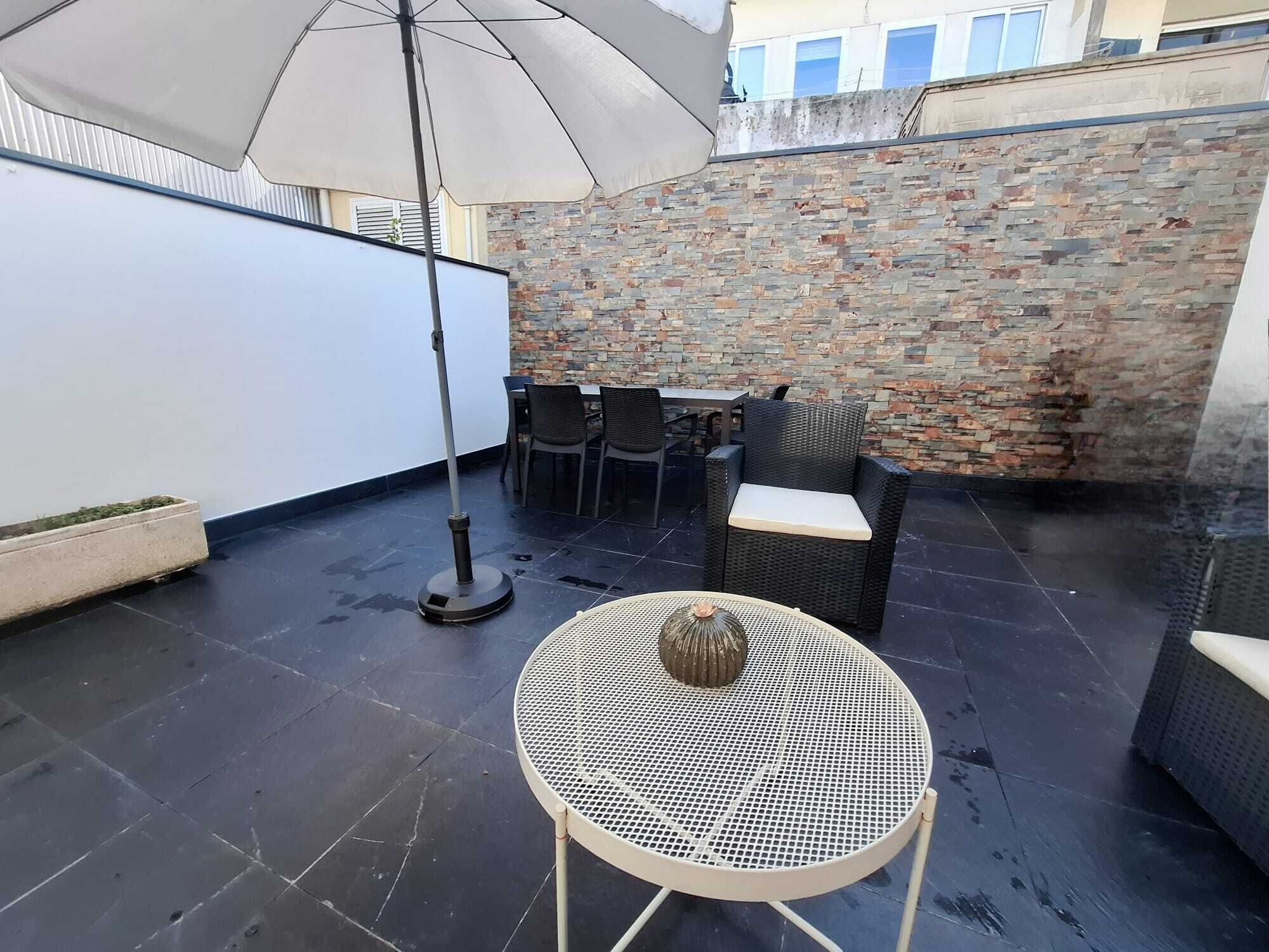 A rooftop patio with a round metal table, wicker chairs, and a large umbrella.